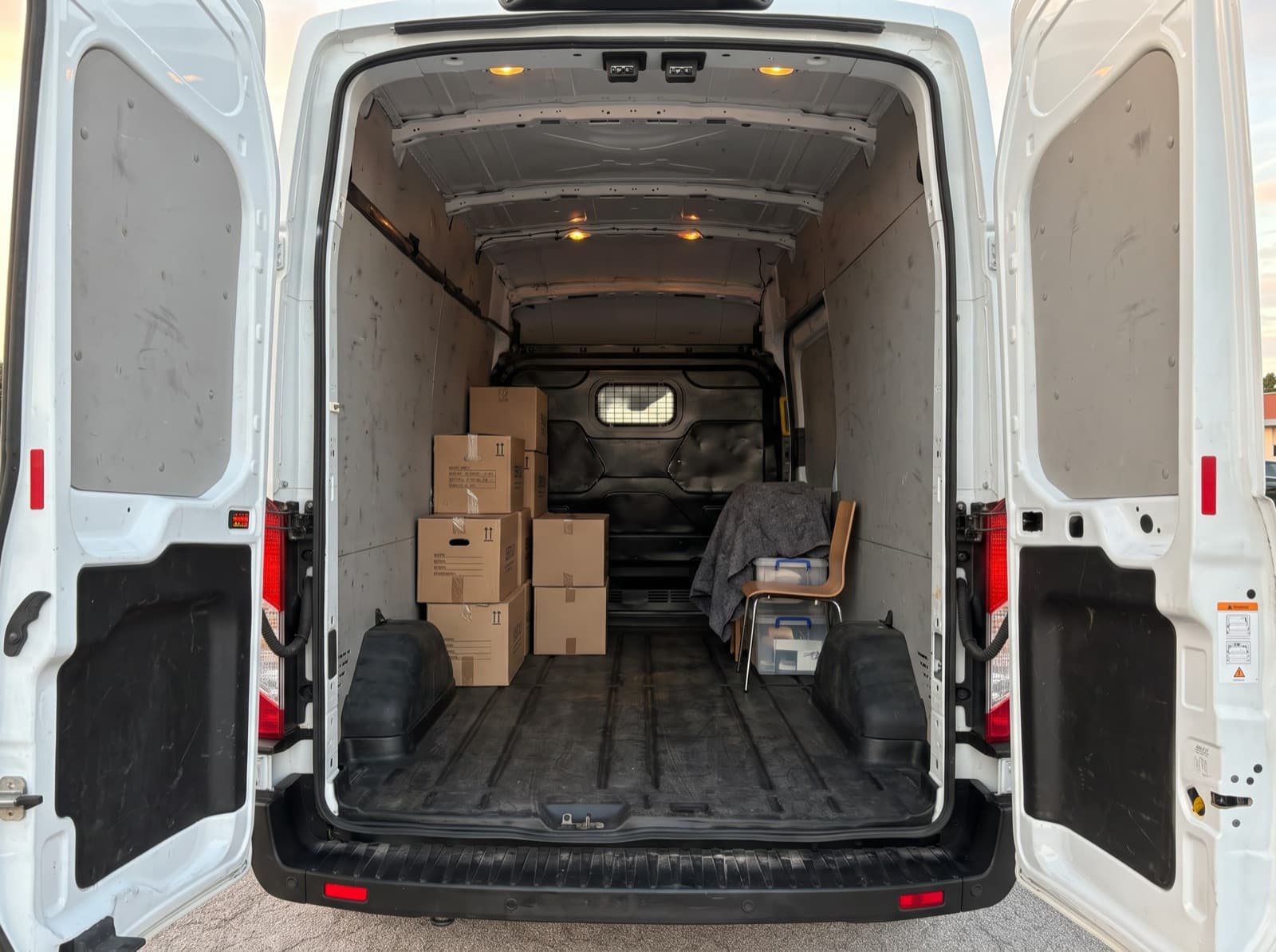 Vano di carico del Ford Transit con le porte posteriori aperte, scatoloni e una coperta protettiva